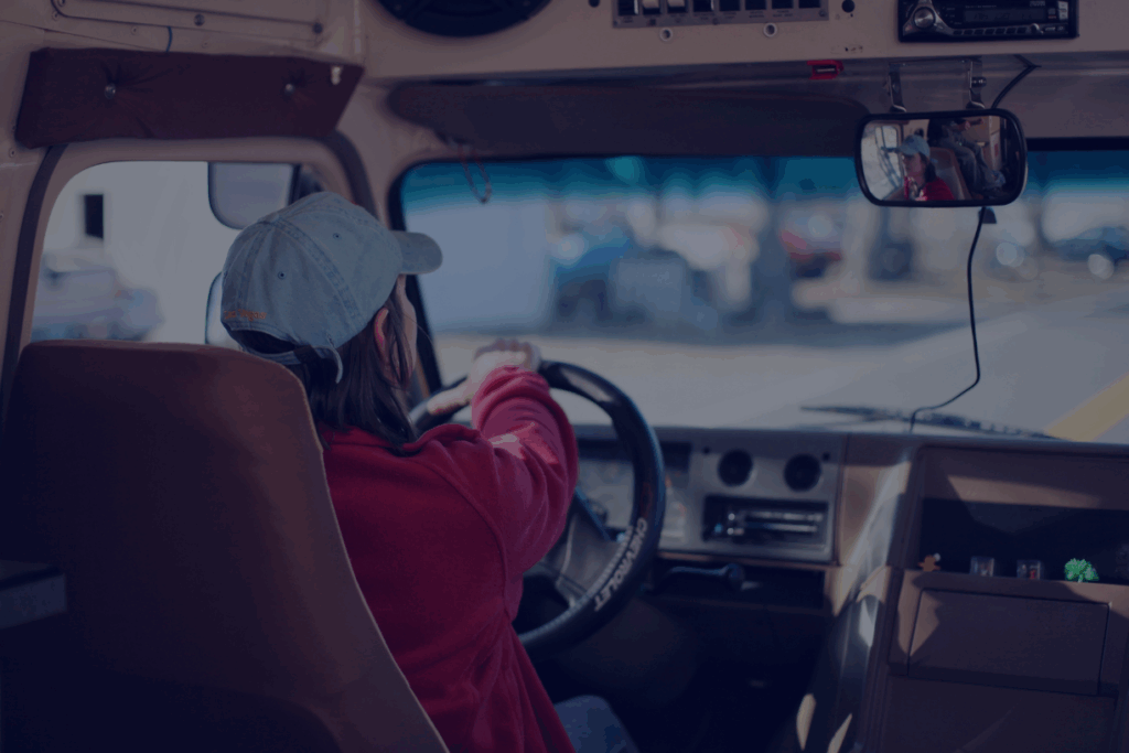 woman with brown hair in a white baseball cap driving an eighteen wheeler truck